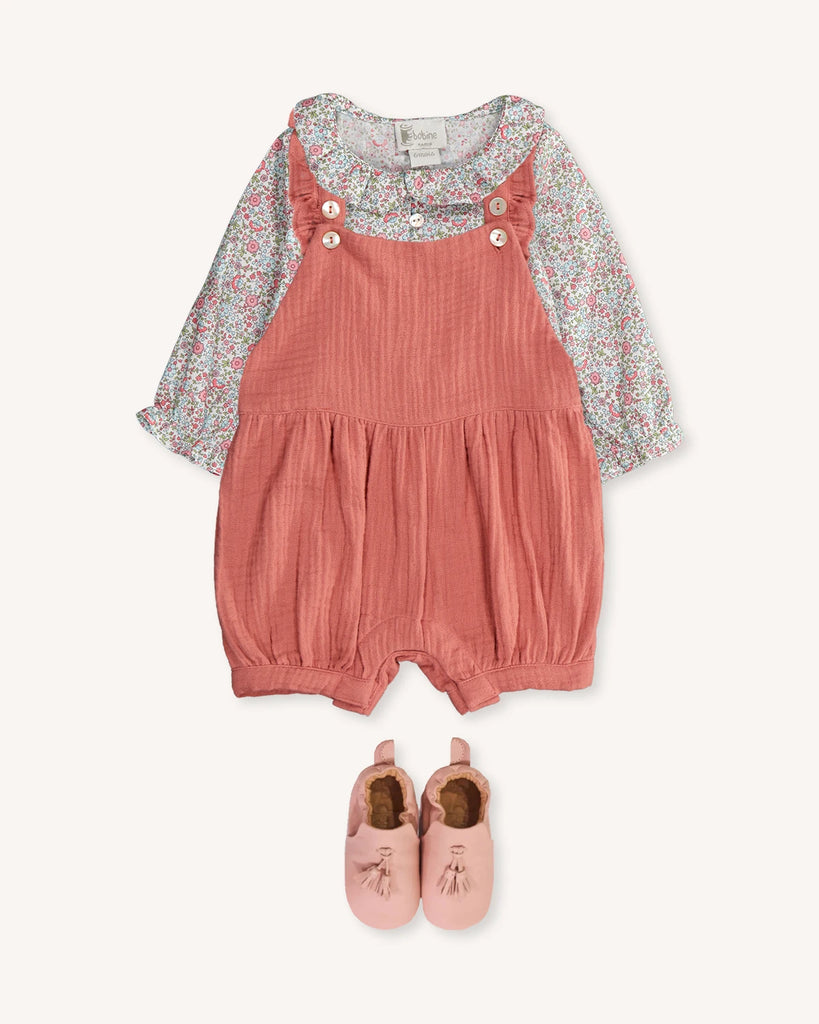 Look pour bébé fille composé de la blouse fleurs printanières, de la salopette en gaze de coton vieux rose et de chaussons en cuir rose à pompons de la marque Bobine Paris.