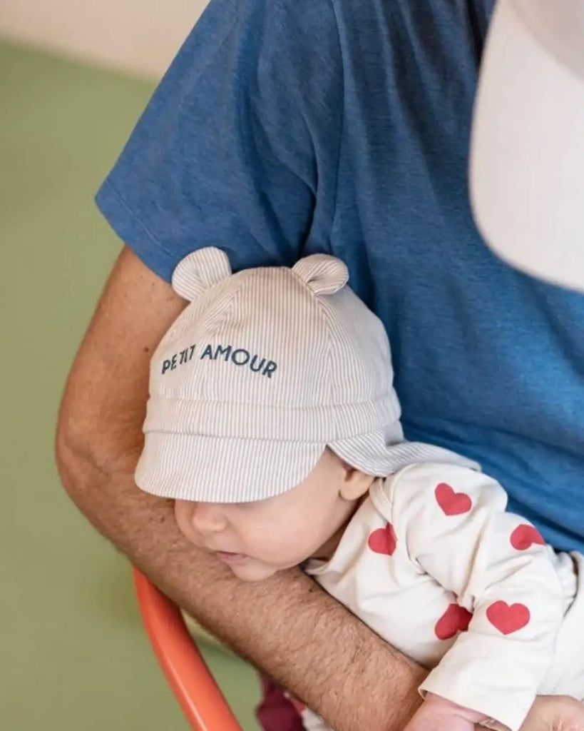 Vue portée du chapeau pour bébé à rayures beiges et broderies bleues "Petit amour" de la marque Bobine Paris.