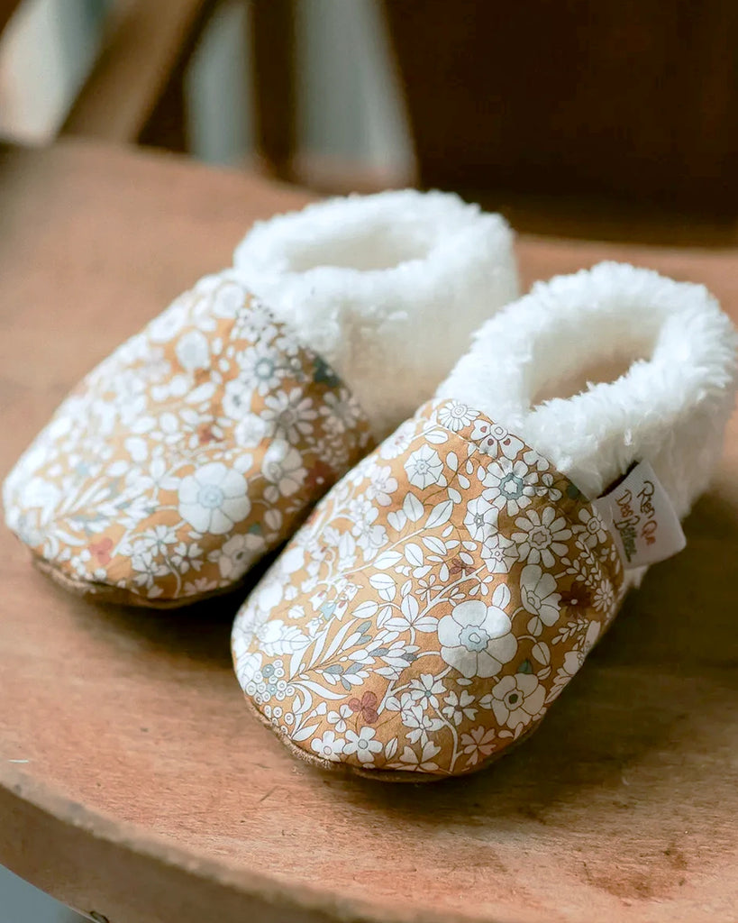 Zoom sur les chaussons pour bébé couleur curry à imprimé fleuri et moumoute de la marque Bobine Paris.