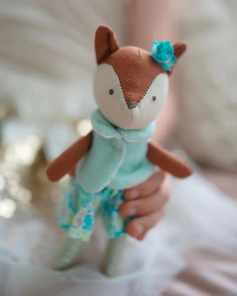 Image d'une peluche renard en habit turquoise pour bébé de la marque Bobine Paris tenue par une main d'enfant.