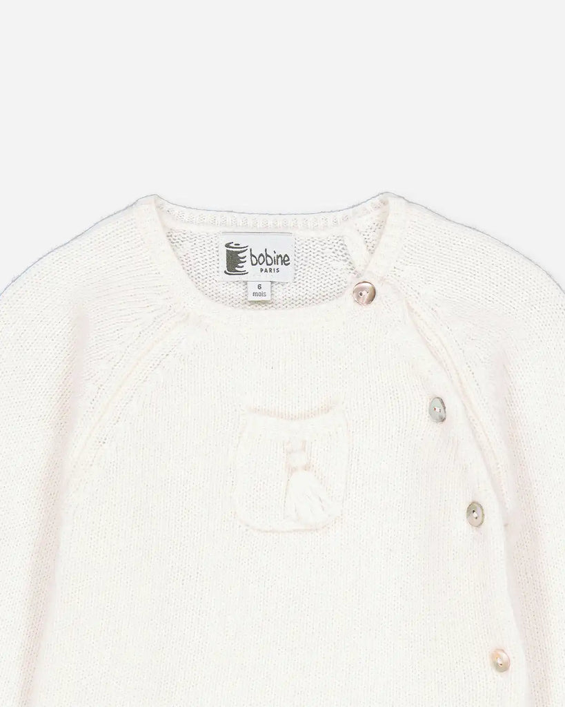 Zoom du pull bébé cache-coeur avec un pompon à l'avant écru de la marque Bobine Paris.