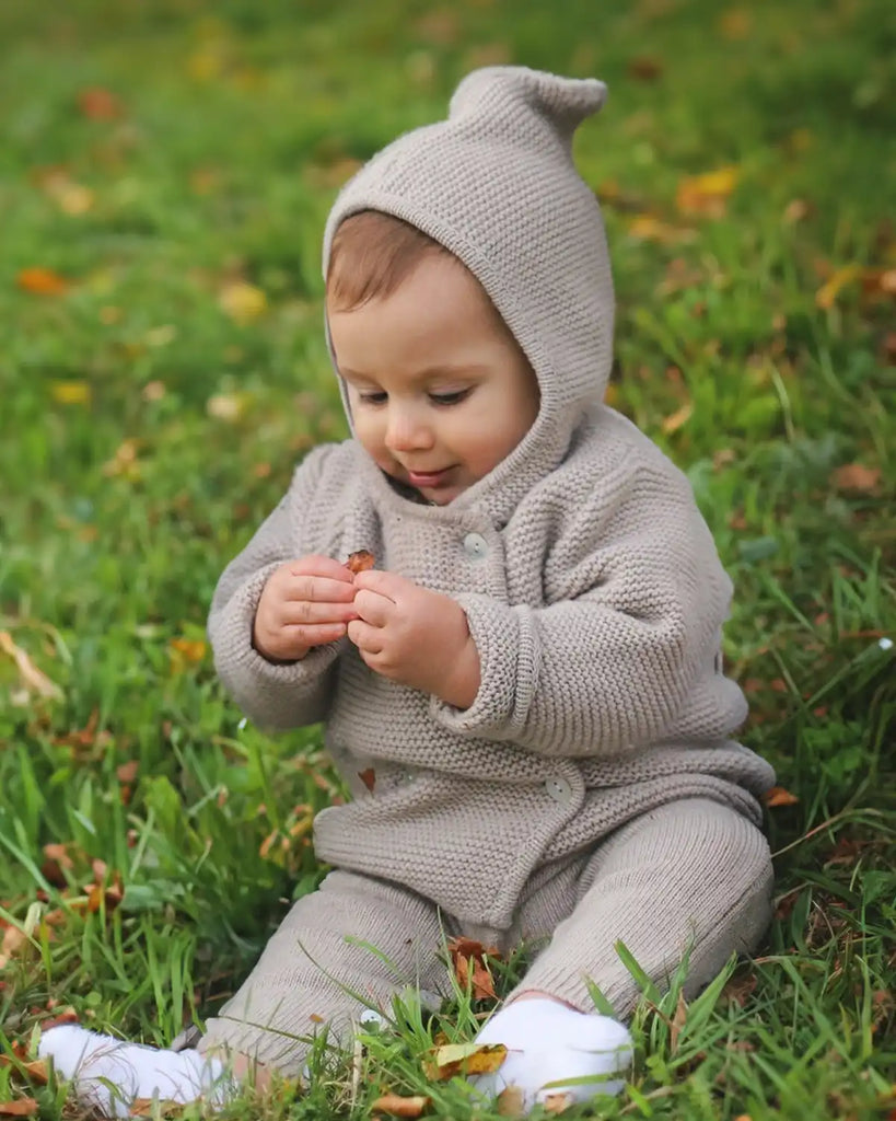 Photo d'un enfant dehors portant la veste bébé à capuche en maille beige clair de la marque Bobine Paris avec un pantalon en maille.