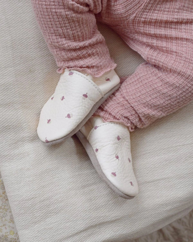 Chaussons pour bébé en cuir souple écru à imprimé de la marque Bobine Paris porté avec un petit pantalon rose.