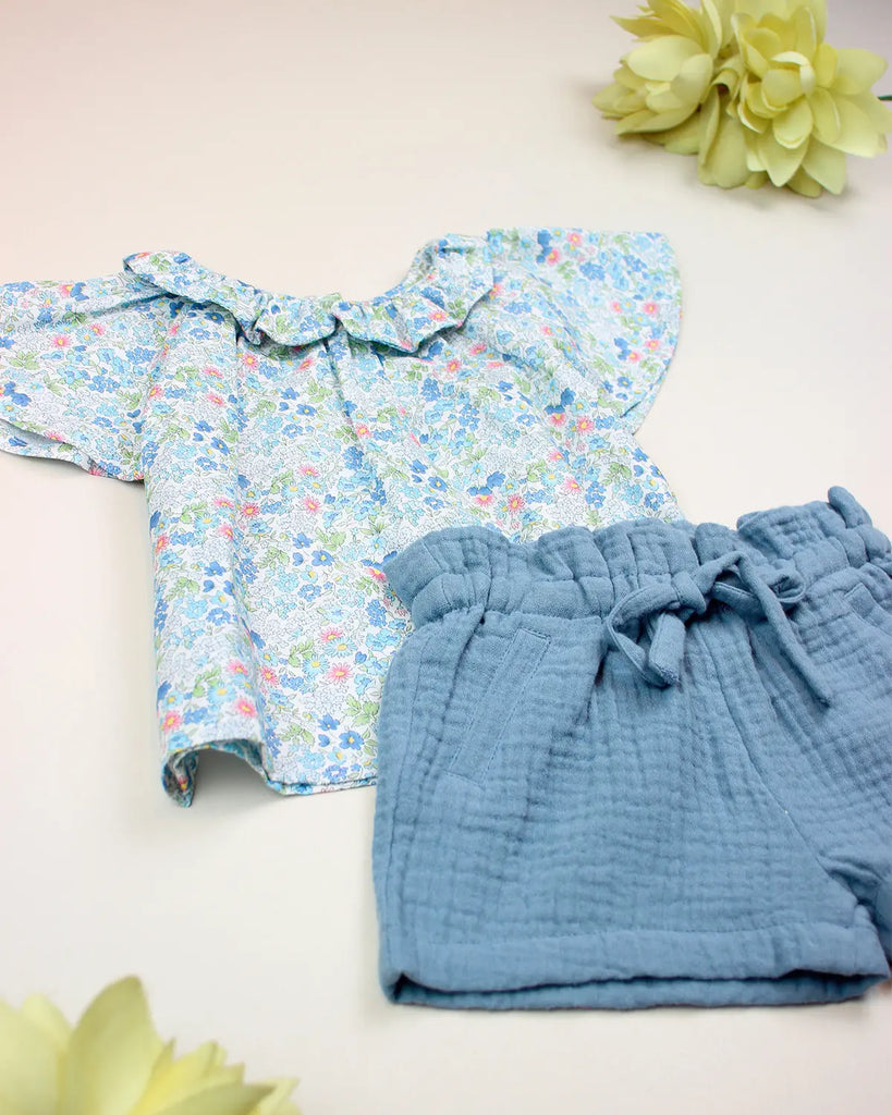 Vue du look pour bébé composé d'une blouse fleurie bleue à col volanté et d'un short en gaze de coton de la marque Bobine Paris.