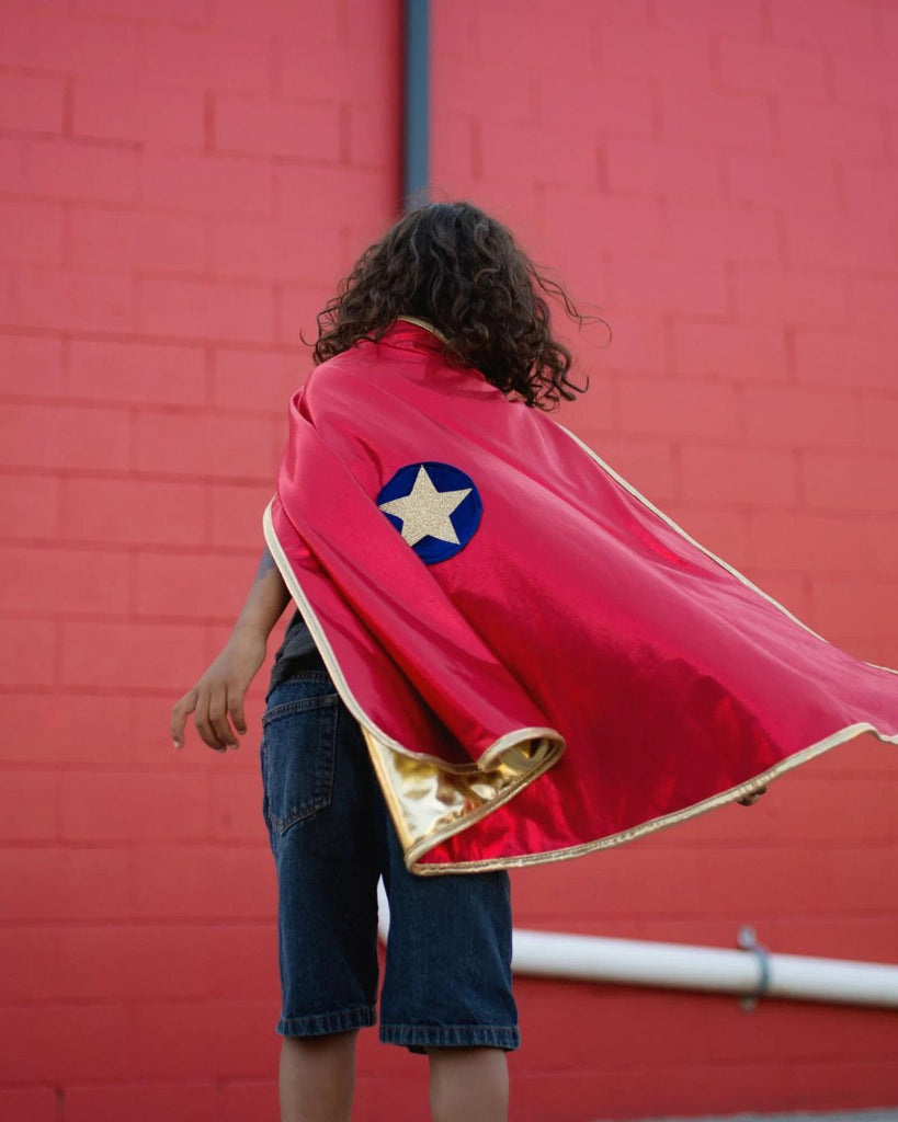 Petit garçon portant une cape de super-héros rouge réversible à doré avec un écusson d'étoile dorée sur fond bleu