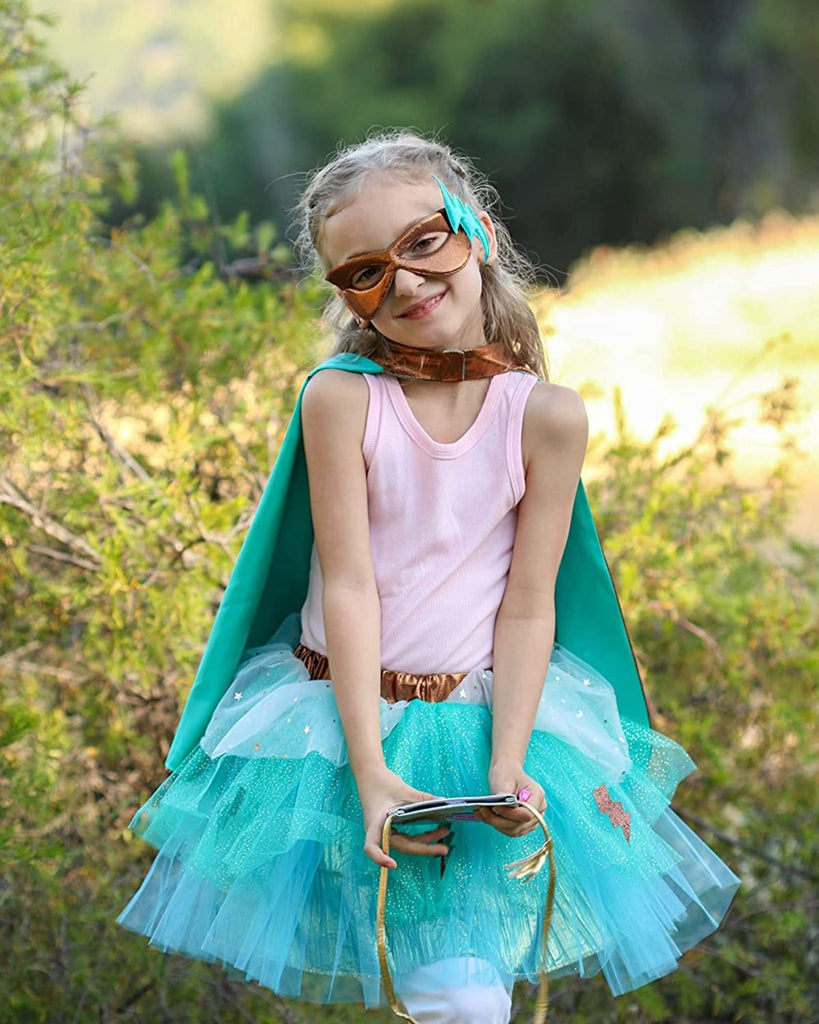 Petite fille portant un déguisement turquoise, doté d'une cape réversible turquoise et métallique cuivrée avec un masque métallique cuivré, et une jupe en tulle turquoise