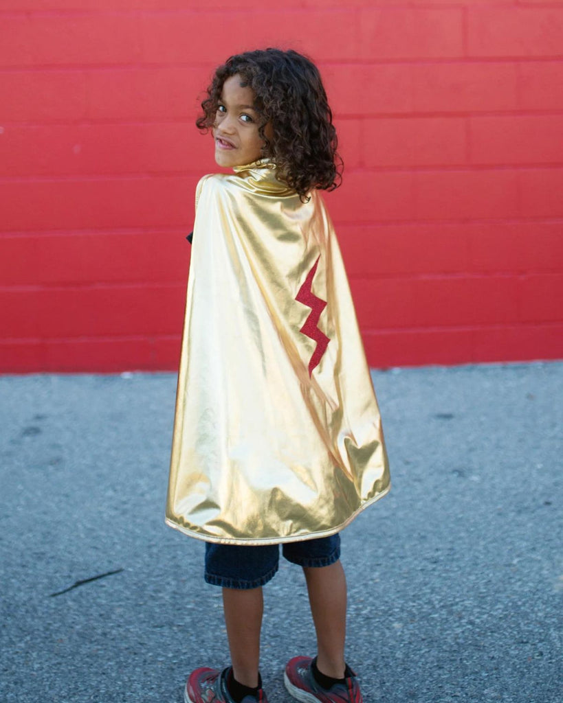 Petit garçon portant une cape de super-héros dorée réversible à rouge avec un écusson d'éclaire rouge