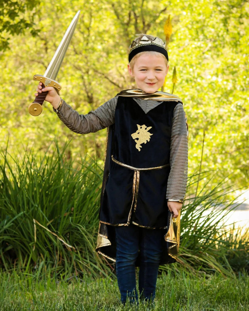 Petit garçon portant un déguisement de chevalier composé d'une tunique noire, d'une cape métallisée dorée et d'une couronne