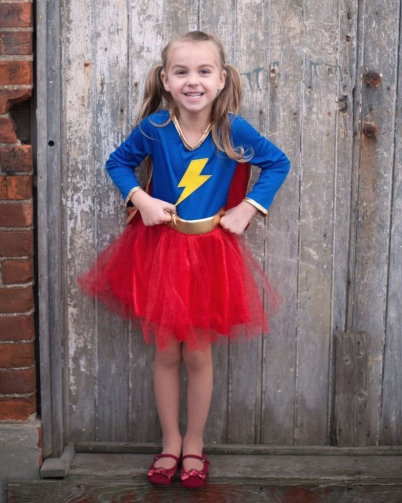 Petite fille portant un déguisement de super-héroine avec un haut bleu et une jupe en tulle rouge. Un éclair jaune peut être vu au centre du haut.