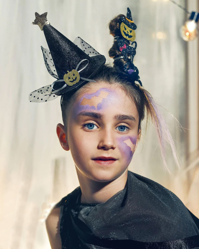 Petite fille portant un serre-tête de de chapeau de sorcière noir avec une citrouille au milieu et une étoile au bout