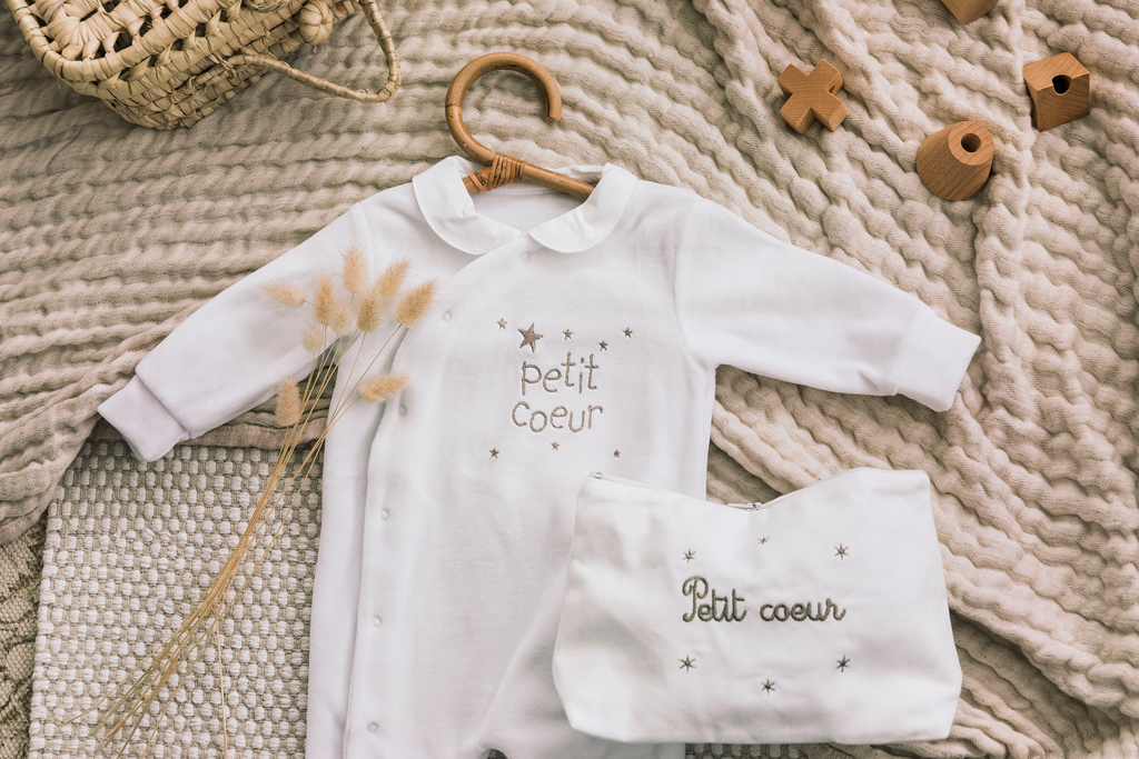 Image d'un coffret de naissance à offrir comprenant un pyjama et une trousse de toilette brodés avec l'inscription 'Petit cœur'.