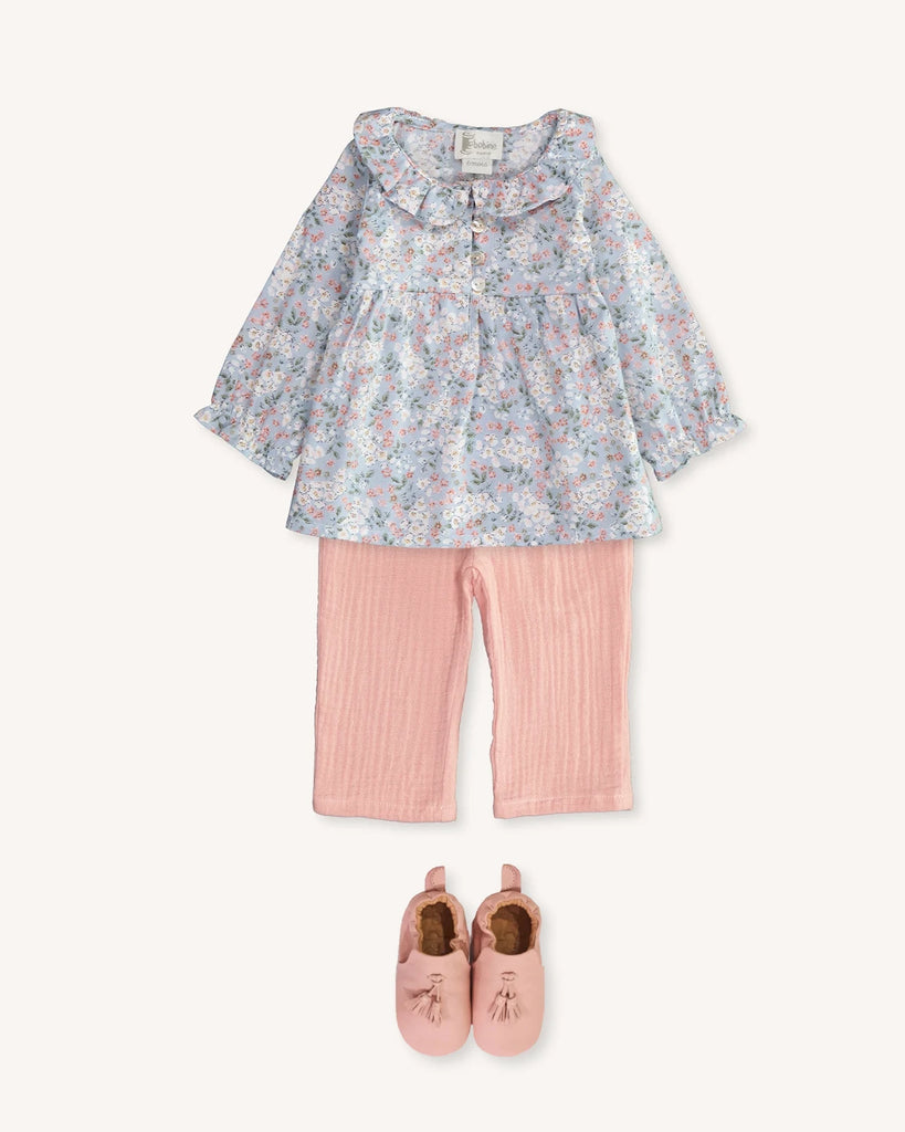 Look pour bébé fille composé d'une blouse bleue fleurie, d'un pantalon en gaze de coton rose et de chaussons en cuir rose à pompons de la marque Bobine Paris.
