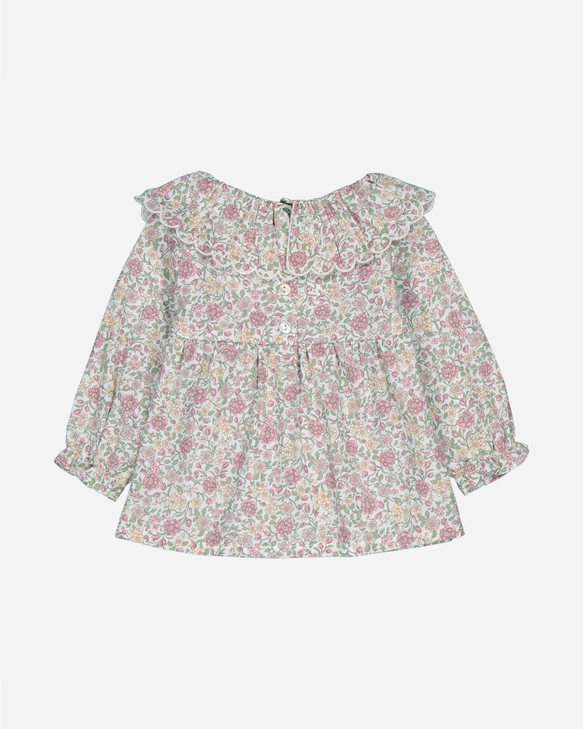 Dos d'une blouse blanche à imprimés de fleurs mauves.
