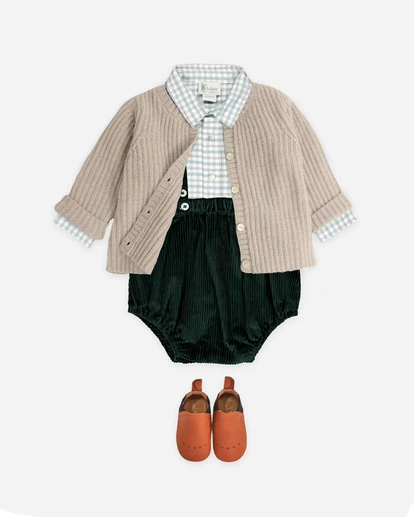 Idée de look contenant le cardigan cotelé unisexe à col rond beige clair pour bébé en laine et cachemire de la marque Bobine Paris avec une chemise à carreau et un bloomer en velours verts à bretelles.