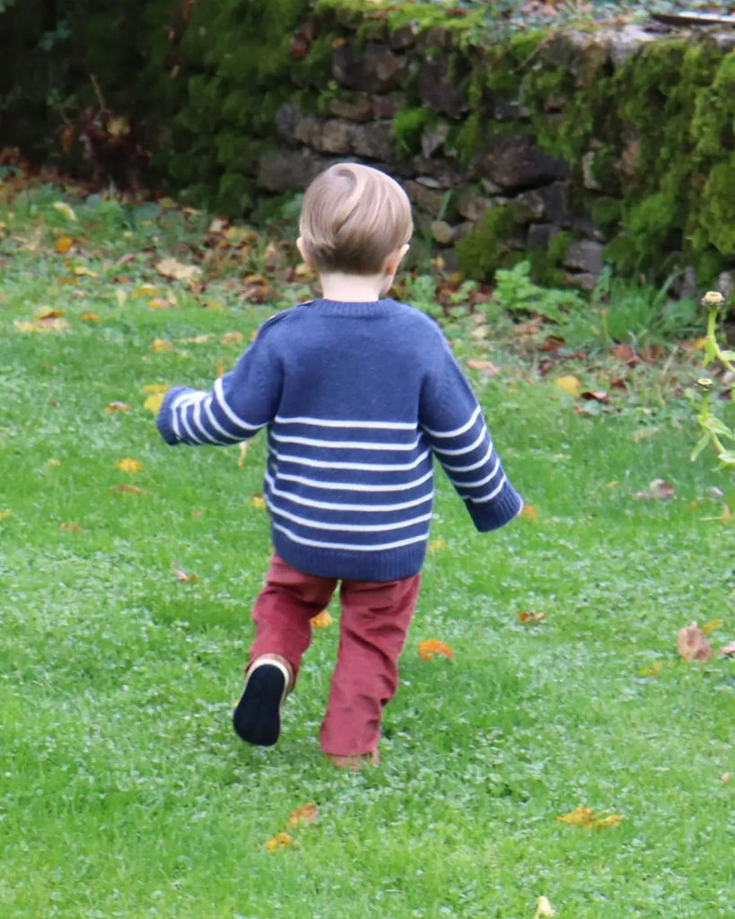 Image d'un enfant jouant tout en portant le pull bébé bleu à rayures blanches en laine et cachemire de la marque Bobine Paris avec un pantalon rouge.