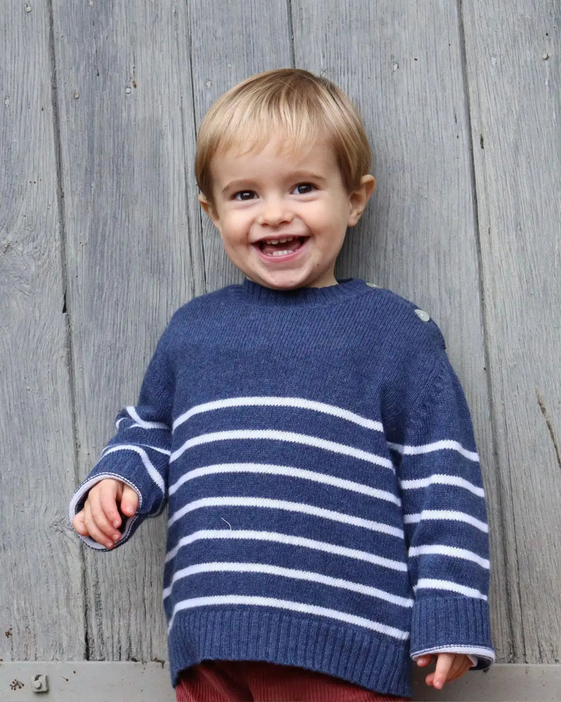 Image d'un petit garçon garçon souriant en portant le pull bébé bleu à rayures blanches en laine et cachemire de la marque Bobine Paris