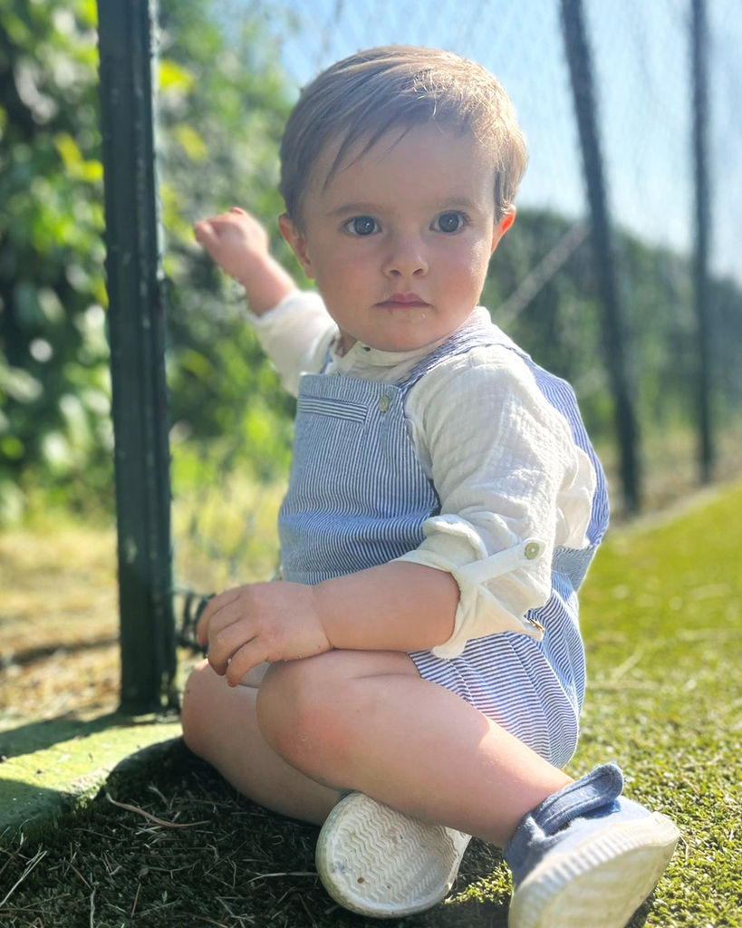 Look porté composé d'une salopette courte à rayures bleues et d'une chemise en gaze de coton retroussée aux manches pour bébé garçon (vue de coté).