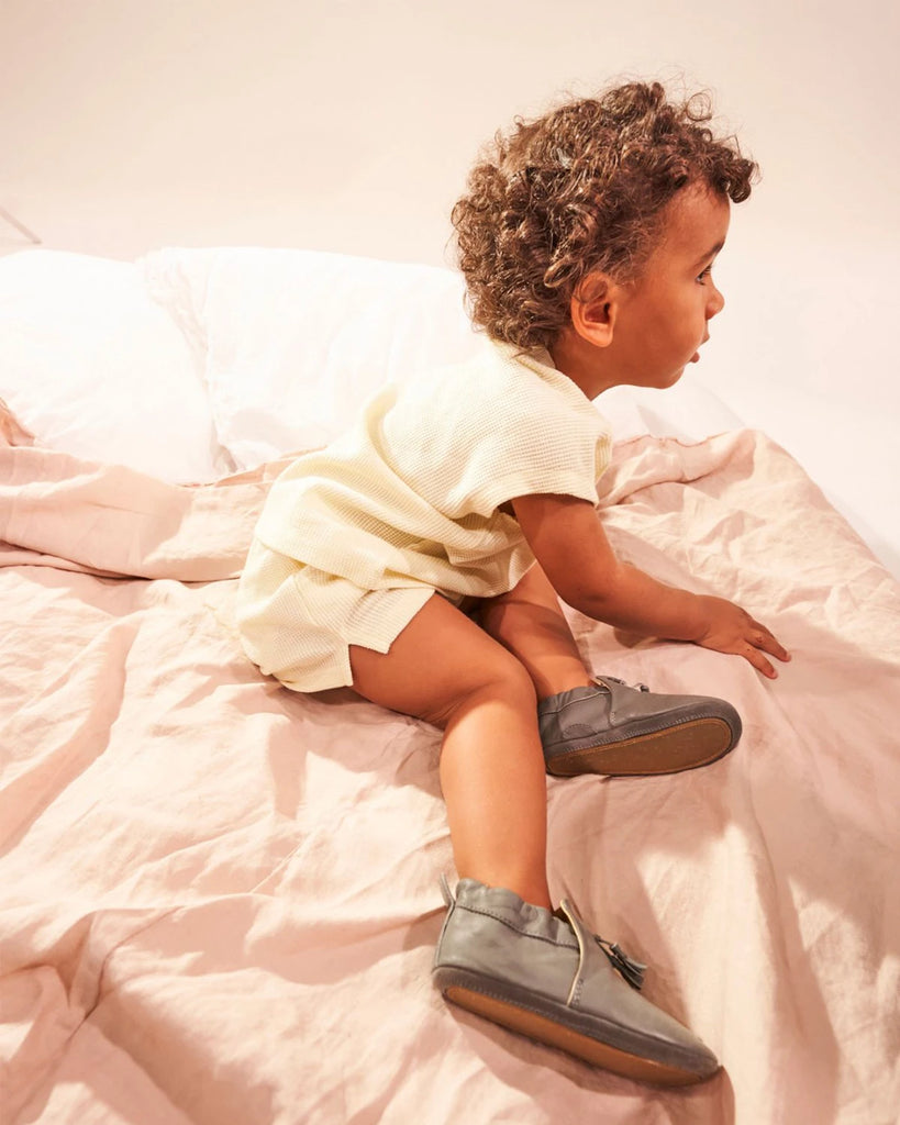 Chaussons pour bébé en cuir gris à pompon de la marque Bobine Paris portés par un bébé.
