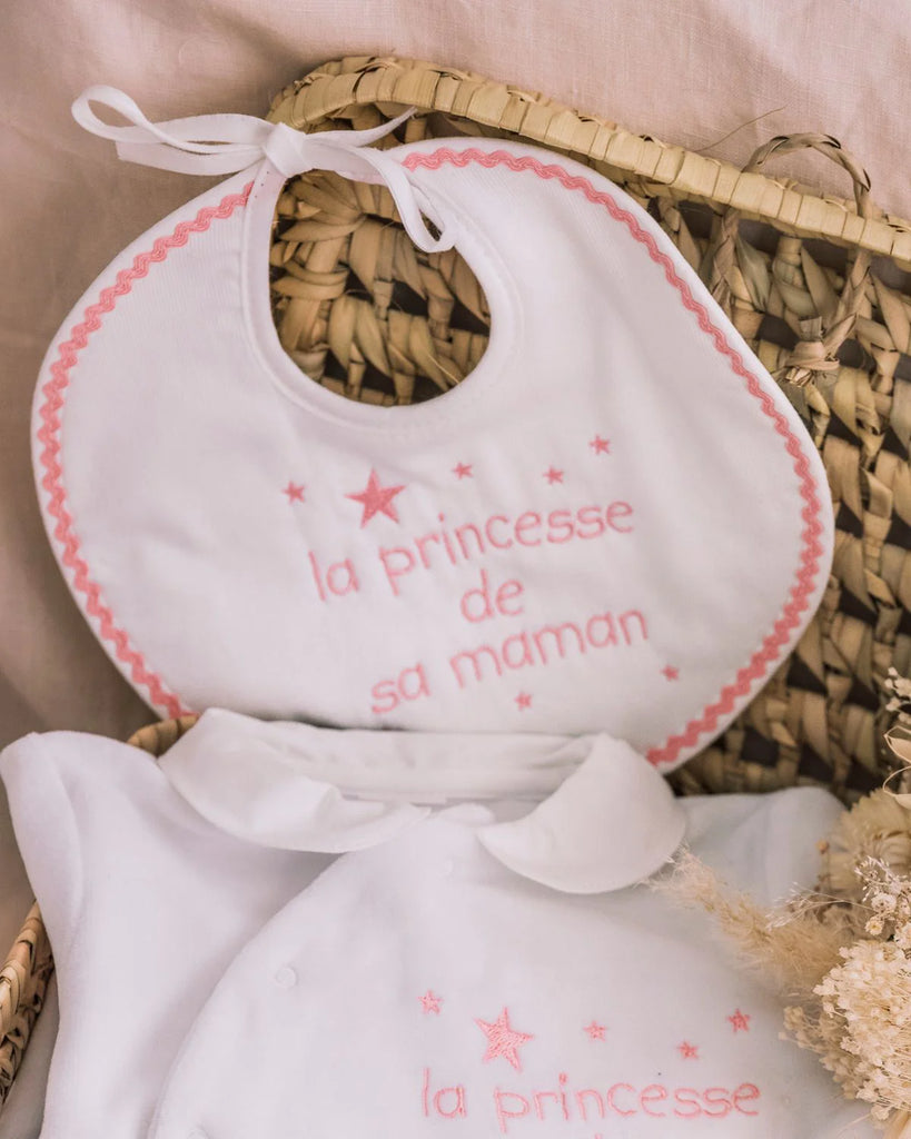 Image du bavoir blanc brodé 'la princesse de sa maman' avec des étoiles et les finitions en rose de la marque Bobine Paris avec un body blanc assorti.