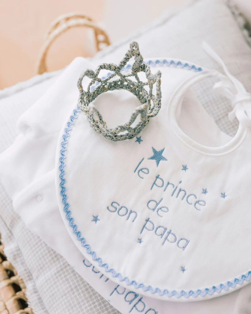 Bavoir blanc brodé 'le prince de son papa' avec des étoiles et les finitions en bleu ciel de la marque Bobine Paris avec un body assorti et une petite couronne en crochet.