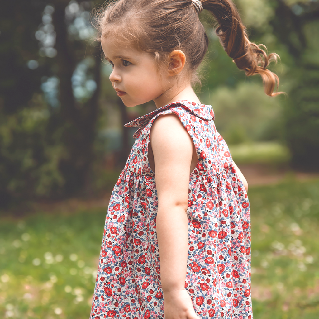 Petit fille qui porte la robe Suzette Bobine imprimée fleurs d'été rouges et bleues