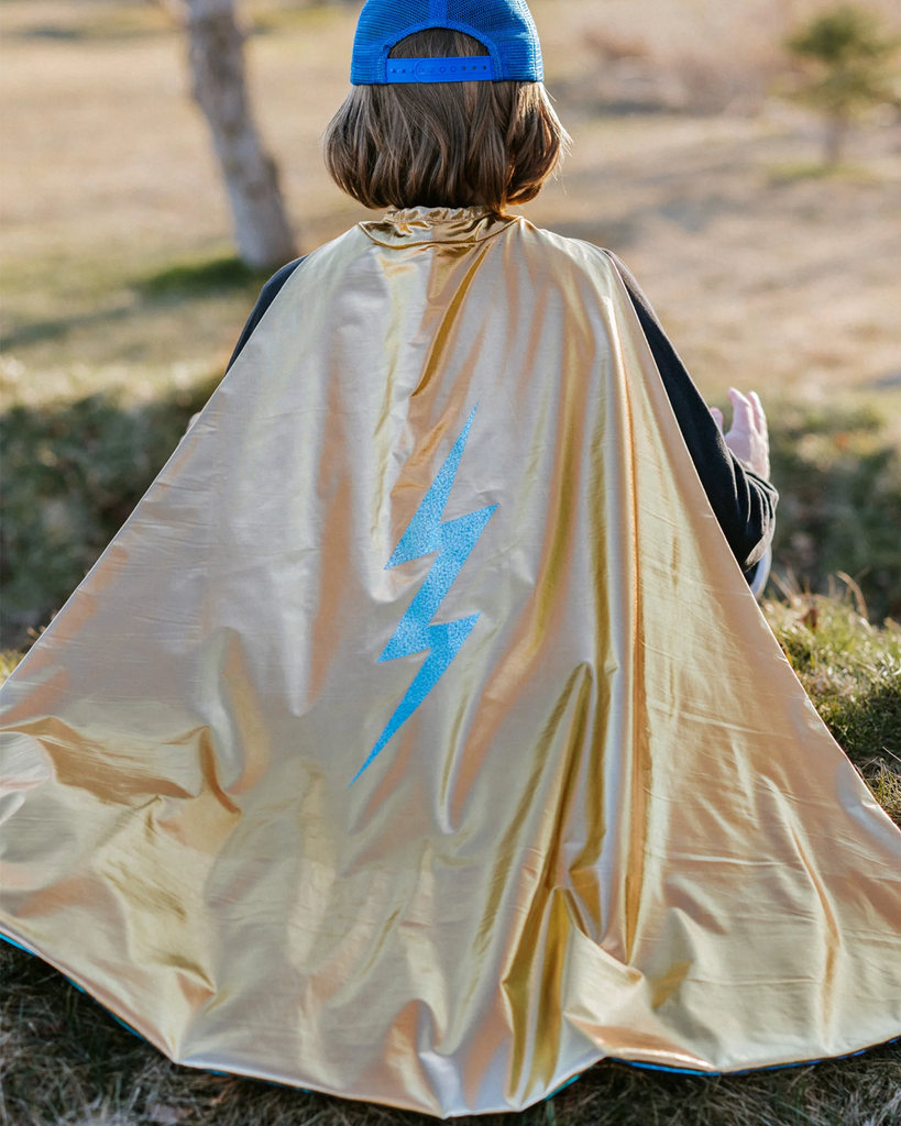 Enfant portant une cape de super-héros dorée métallique avec un éclair bleu sur le dos