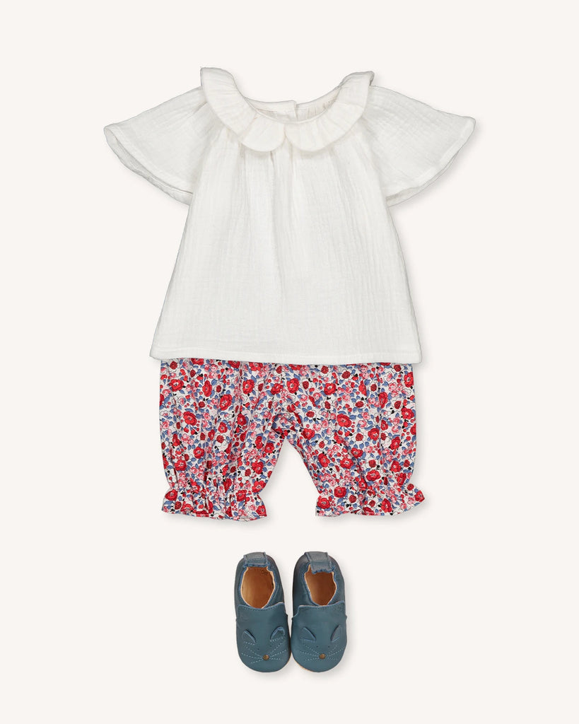 Look pour bébé composé d'une blouse en gaze de coton blanc, d'un panty à fleurs rouges et de petits chaussons bleus de la marque Bobine Paris.