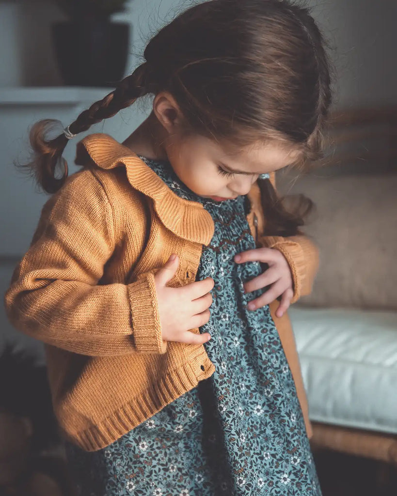 Image d'une petite fille portant le cardigan à col volanté sablé et la robe Mia smockée fleurs turquoises Bobine Paris