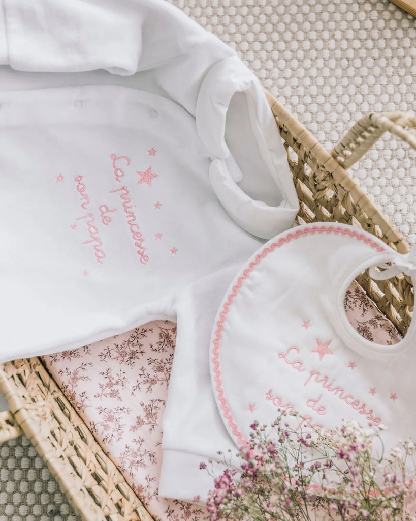 Vue du pyjama en coton blanc à broderies rose "La princesse de son papa" de la marque Bobine Paris avec un bavoir assorti.