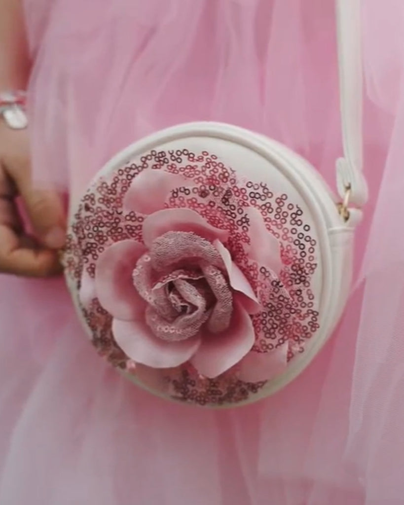 Petite fille portant un sac rond blanc avec une rose de couleur rose ornée de pailletes roses