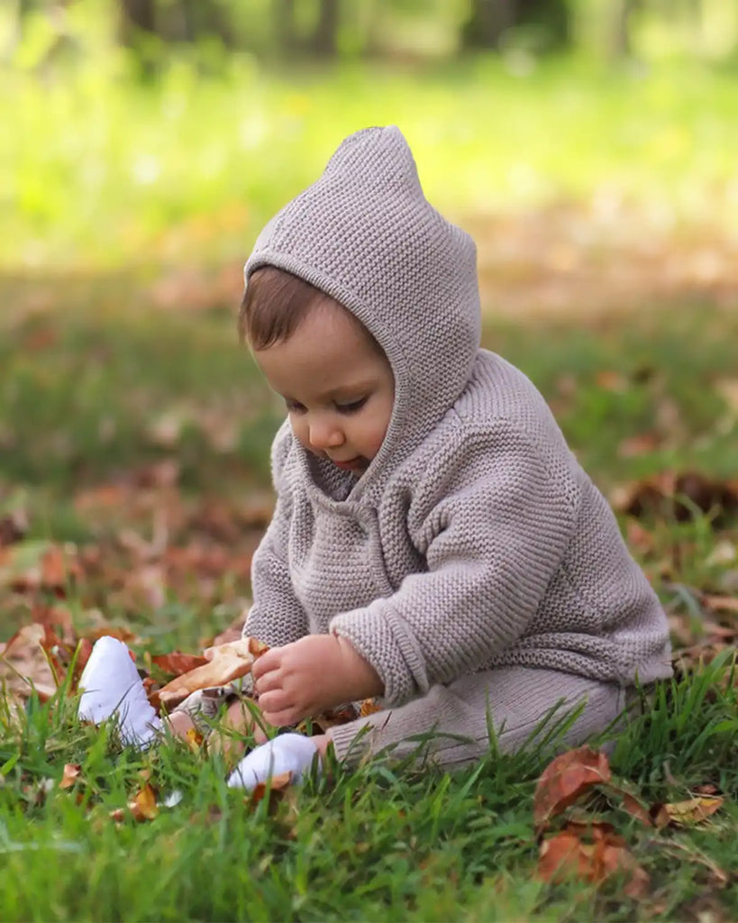 Photo d'un enfant jouant dehors en portant la veste bébé à capuche en maille beige clair de la marque Bobine Paris.