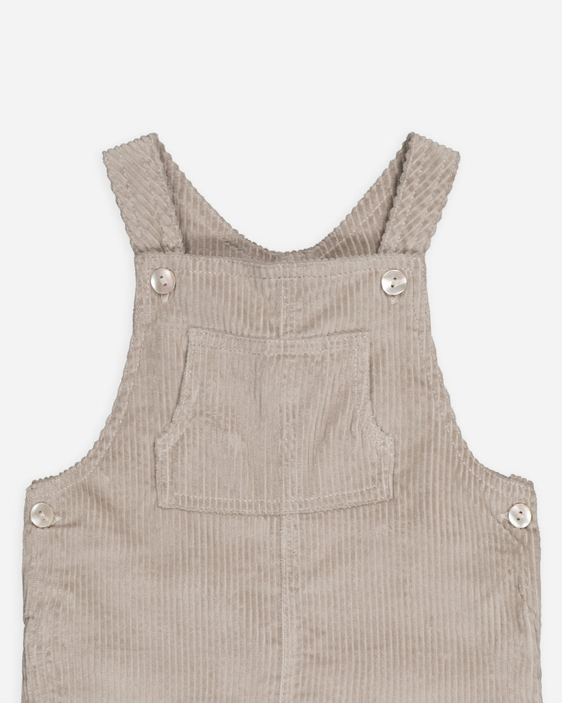 Zoom sur la salopette beige sable velours avec une poche au centre de la poitrine et quatre boutons nacrés.