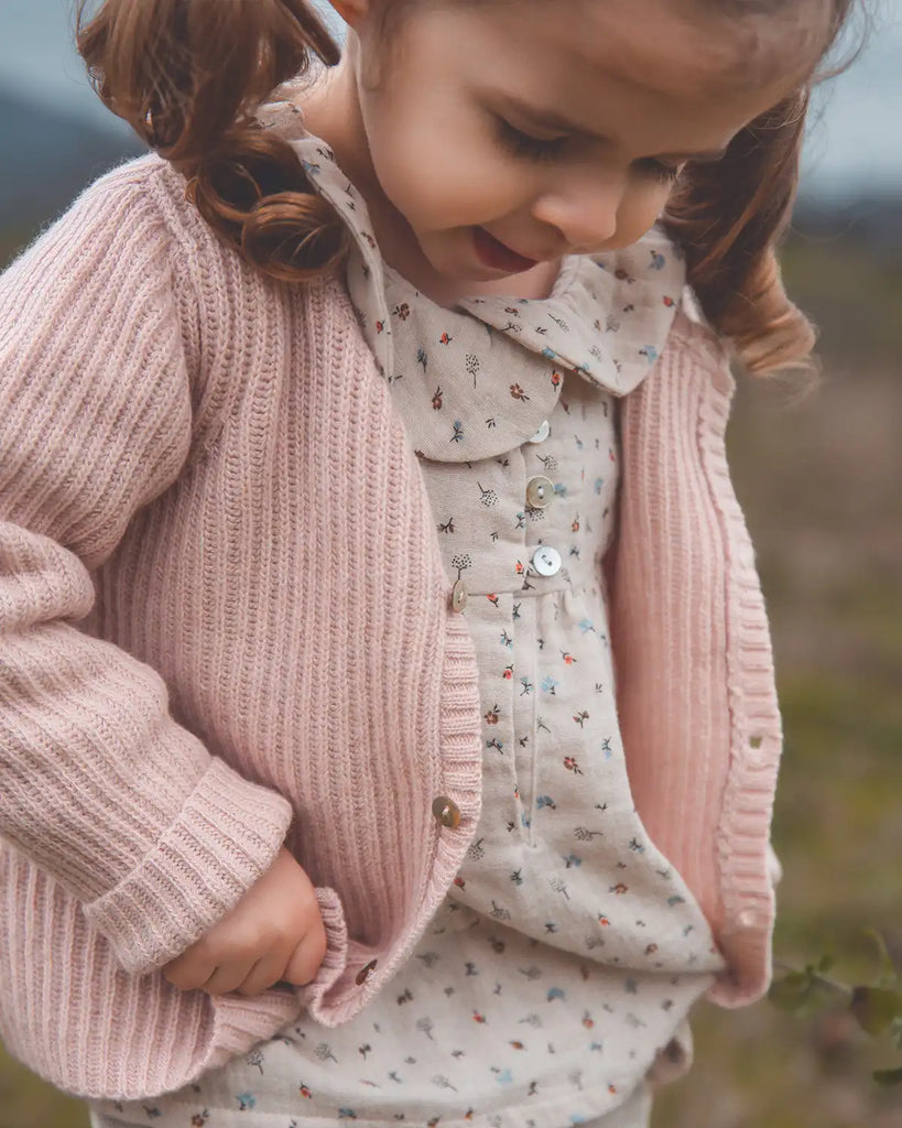 Zoom d'une petite fille portant le cardigan à col rond bébé côtes rose poudre Bobine Paris