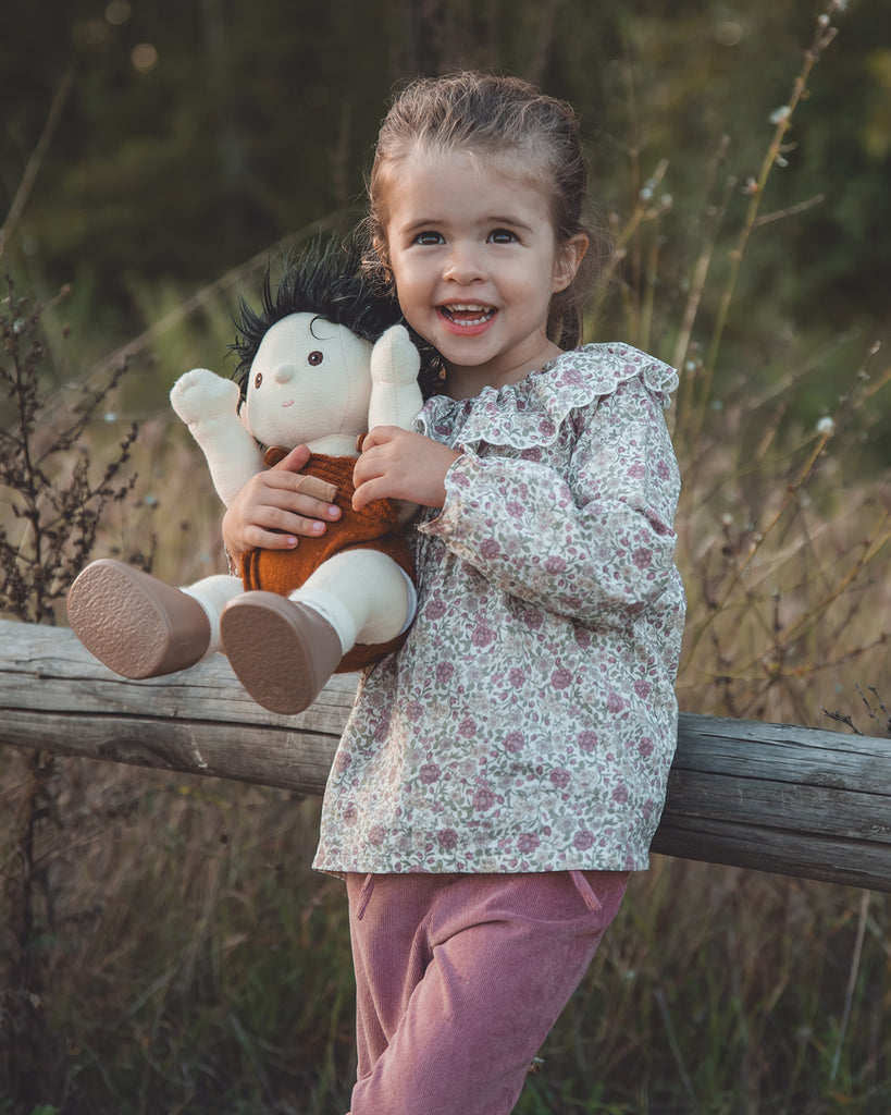 Petite fille portant une blouse à imprimés mauves doté d'un col volant avec un pantalon rose. 
