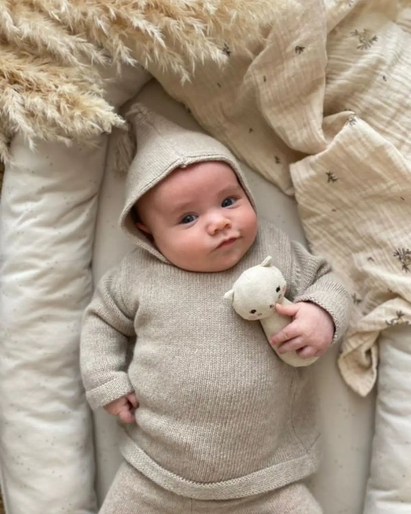 Photo d'un bébé portant le burnous beige layette avec le pantalon assorti en laine et cachemire de la marque Bobine Paris avec un bas assorti.