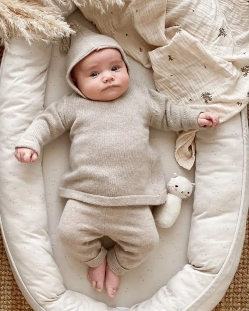 Image d'un bébé portant le burnous beige layette avec le pantalon assorti en laine et cachemire de la marque Bobine Paris.