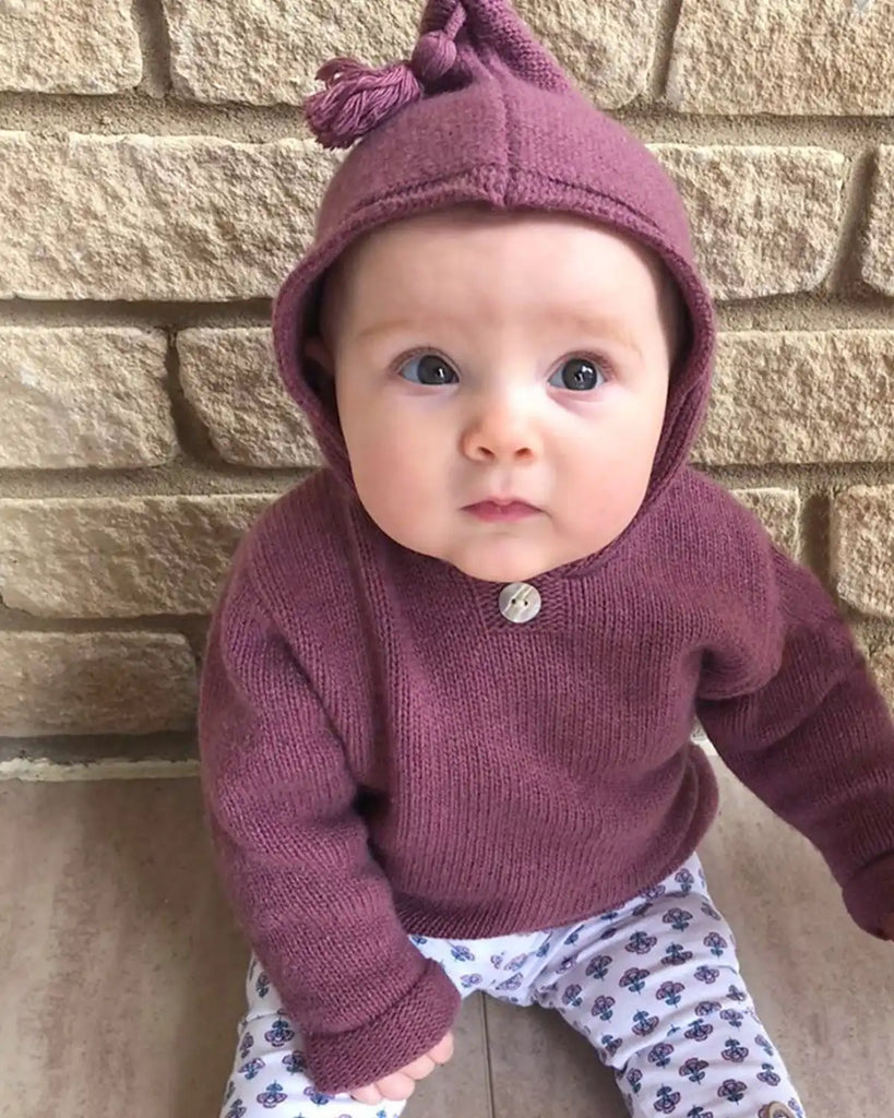 Vue de dos du burnous bébé à capuche parme en laine et cachemire de la marque Bobine Paris porté par un bébé.