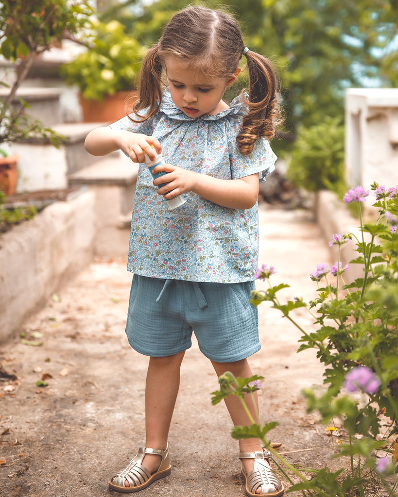 Photo d'une petite fille portant la blouse à col volanté pour bébé fille à motifs fleuris bleus avec un short en gaze de coton bleu de la marque Bobine Paris.