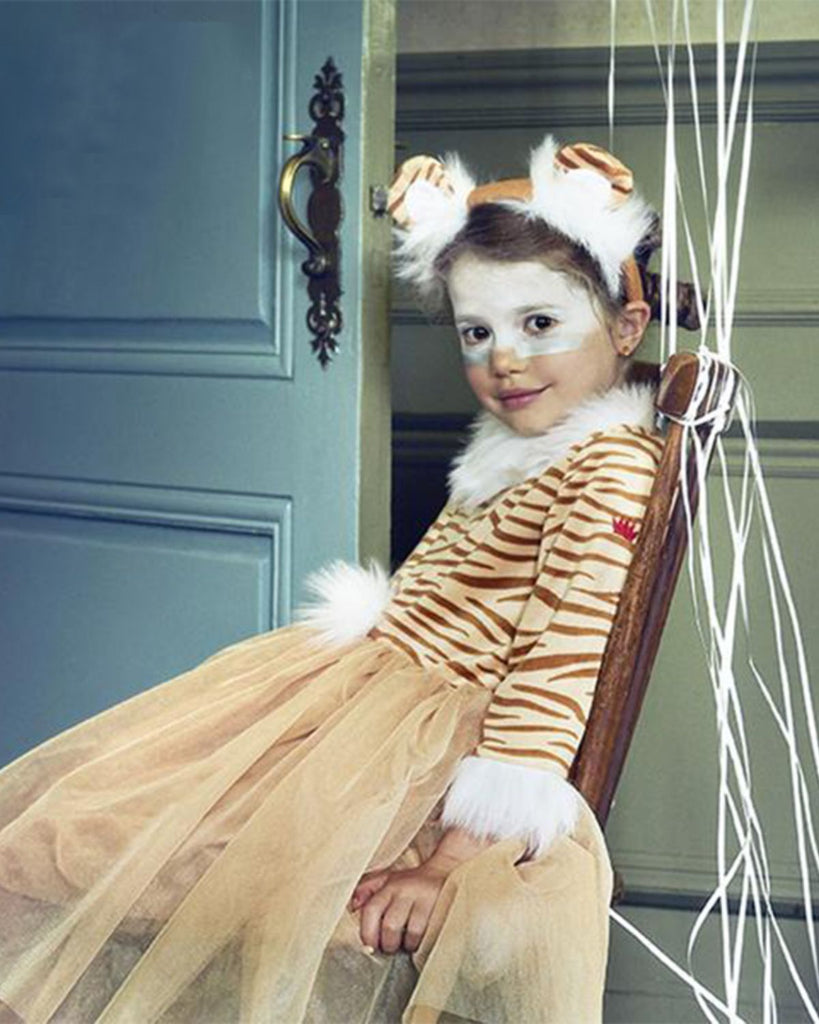 Petite fille portant un déguisement de tigresse à rayures marron sur fond beige avec bas en tulle et serre-tête assorti