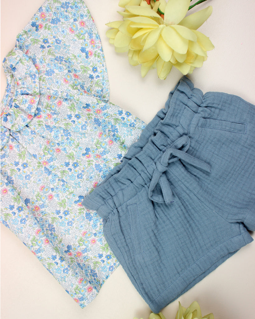 Zoom sur la blouse à col volanté pour bébé fille à motifs fleuris bleus et un short en gaze de coton bleu de la marque Bobine Paris.