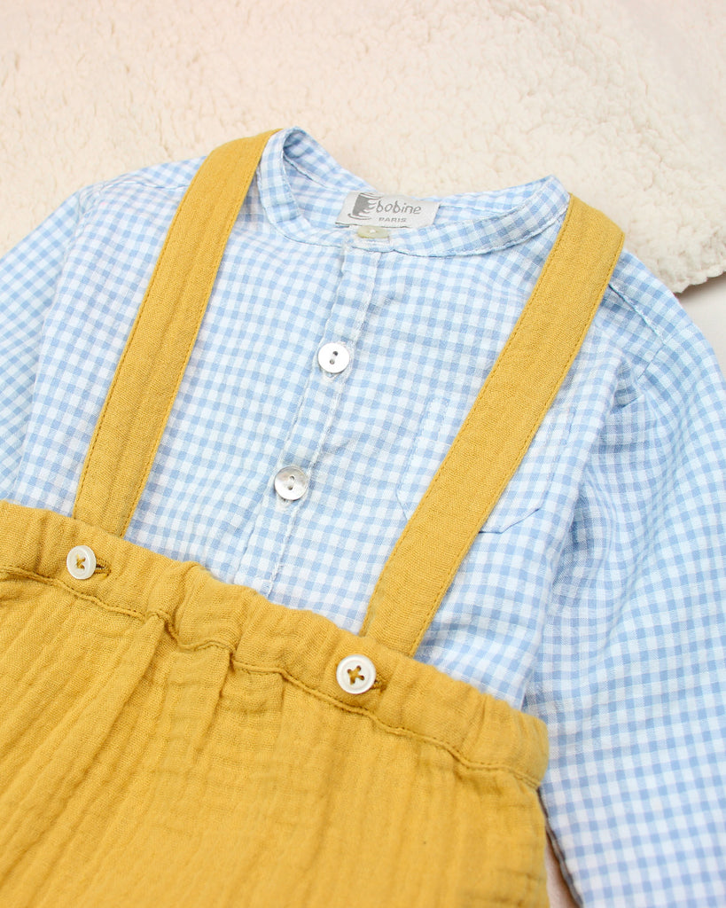 Zoom du bloomer pour bébé à bretelles en gaze de coton couleur curry associé avec une chemise à carreaux bleus de la marque Bobine Paris.
