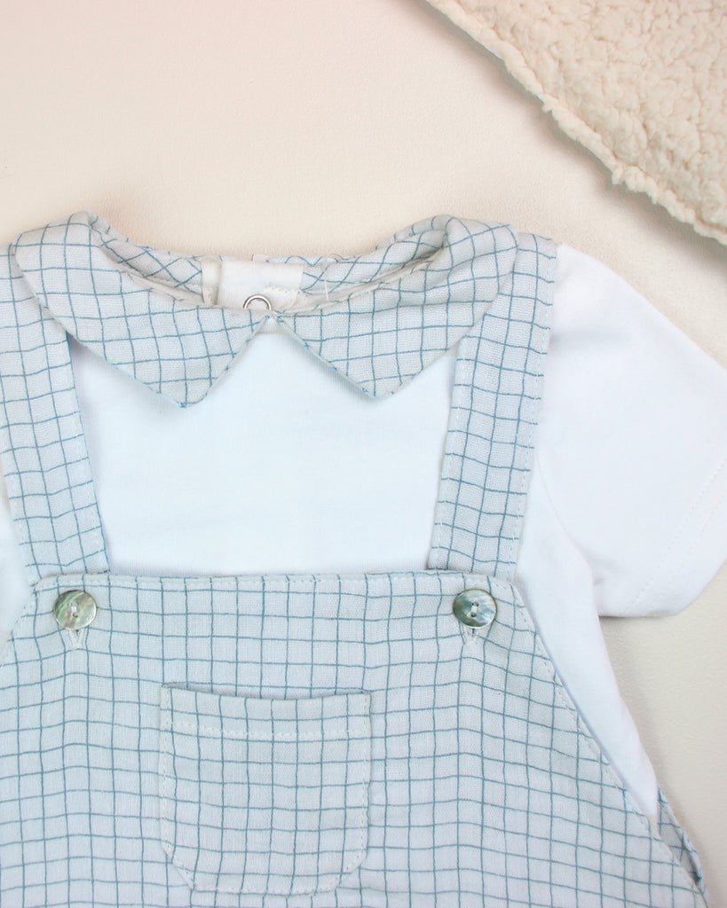 Zoom du look constitué d'une salopette pour bébé garçon à motif quadrillé bleu et d'un t-shirt blanc avec col point assorti de la marque Bobine Paris.